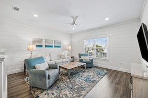 A modern living room with a ceiling fan, a large window with a view, and a blue armchair. - Luxury home with private pool, outdoor kitchen w/fireplace & deeded beach access (Seacrest Beach West)