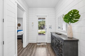 A hallway with a wooden floor, a white door, and a dark wooden cabinet with a plant on top.