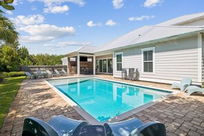 Une piscine avec des chaises longues, un espace barbecue et un patio couvert.