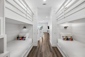 Passadís estret amb parets blanques i terra de fusta, que condueix a una habitació amb un llit i un televisor fixat a la paret.
