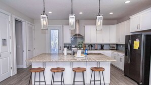 Una cocina moderna con una isla central, taburetes de bar, lámparas colgantes y un refrigerador negro.