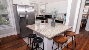 A kitchen with white cabinets, stainless steel appliances, a granite countertop, and wooden stools.