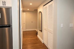 A hallway with a stainless steel refrigerator, a white door, and a set of white louvered closets.