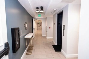 Un couloir avec une porte blanche, un panneau indiquant la sortie de secours et un détecteur d’incendie sur le mur.