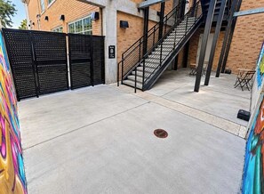 Une cour en béton avec un portail en métal noir, un escalier et une petite table.