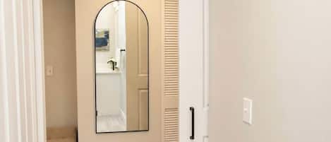 Un pasillo con suelo de madera, una puerta blanca y un espejo en la pared.
