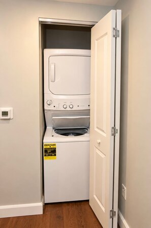 A compact laundry room with a front-loading washer and dryer, a door with a handle, and a wall-mounted thermostat.