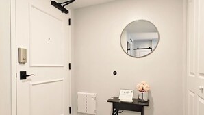A hallway with a white door, a round mirror on the wall, a small table with a vase, and a radiator. - Fun Cozy Studio Apts - 1 Mile to TIAA Bnk Fld! (Jacksonville)