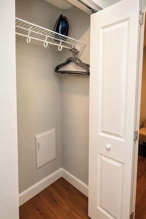 A closet with a white door, a white ceiling-mounted shelf, and a hanging rack.