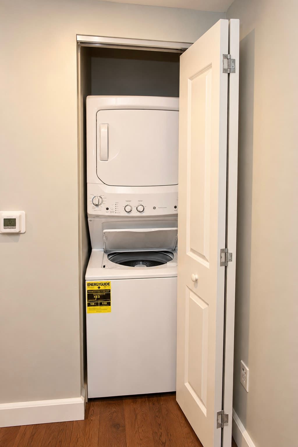 Un lavadero pequeño con lavadora y secadora de carga frontal, una puerta con picaporte y un termostato instalado en la pared.