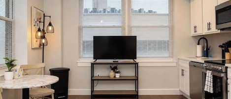 Una cocina moderna con una televisión de pantalla plana, un comedor con mesa y sillas, y una alfombra estampada.