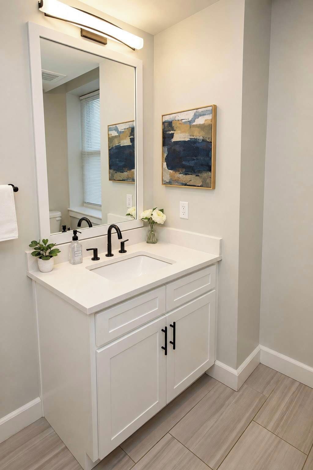 A bathroom with a white vanity, a large mirror, a sink, and a painting on the wall.