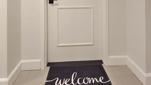 Una puerta blanca con un felpudo que dice 'welcome', un accesorio de iluminación y un timbre.