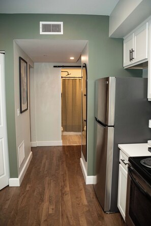 A kitchen with a stainless steel refrigerator, a stove, and a microwave. There is a wooden floor and a window with blinds.