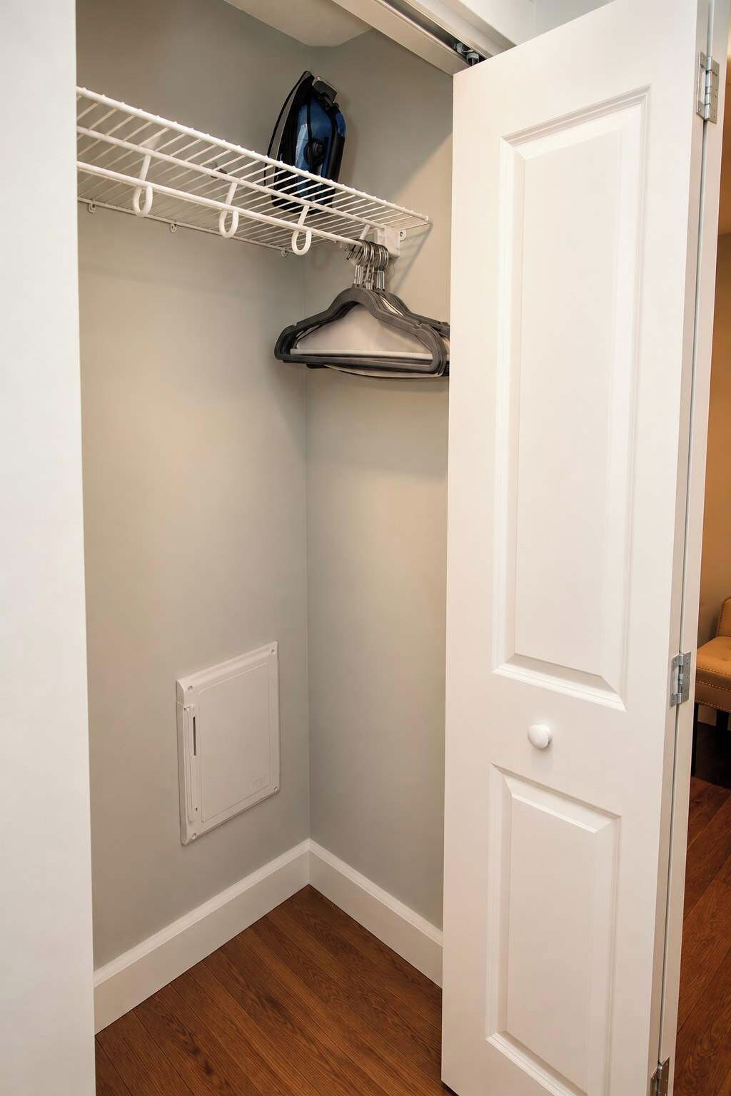 Un armario con puerta blanca, un estante blanco en la pared y una barra para colgar ropa.