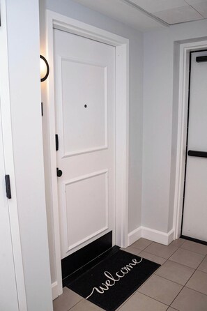 A white door with a black doormat that reads 'welcome' and a light fixture above it. - Fun Cozy Studio Apts - 1 Mile to TIAA Bnk Fld! (Jacksonville)