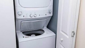 Een kleine, witte wasruimte met een verticaal geplaatste wasmachine en droger.