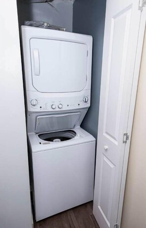 A compact, white laundry room with a washer and dryer stacked vertically. - Elegant 1BR King Bed Apts - 1.3 Miles to TIAA Bnk Fld (Jacksonville)