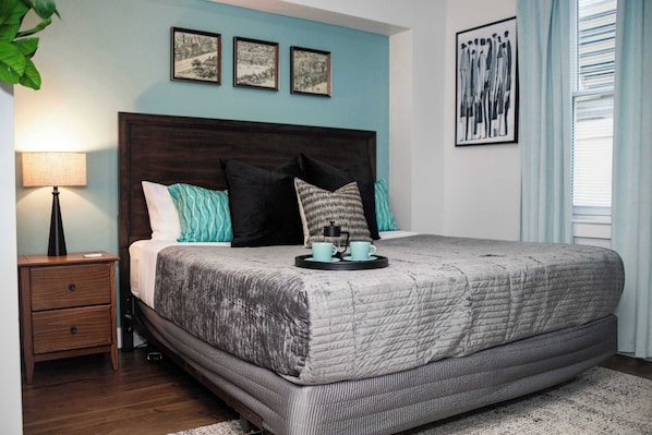 A bedroom with a large bed, a nightstand, a lamp, and a window with curtains.