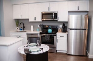A modern kitchen with white cabinets, stainless steel appliances, and a marble countertop with a dining table set for two.