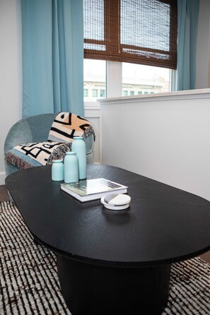 Una habitación moderna con una mesa redonda negra, una silla azul y una ventana con vistas a edificios.