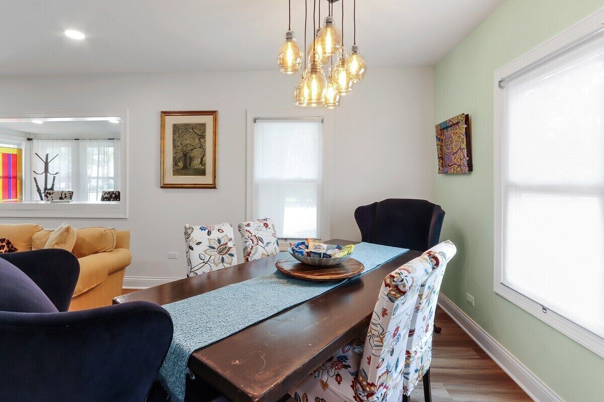 Un coin repas avec une table en bois, des chaises à motifs floraux, un lustre et des œuvres d’art accrochées aux murs.