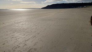 Ein weiter, leerer Strand mit Fußspuren und einem Blick auf das Meer und einen Hügel in der Ferne.