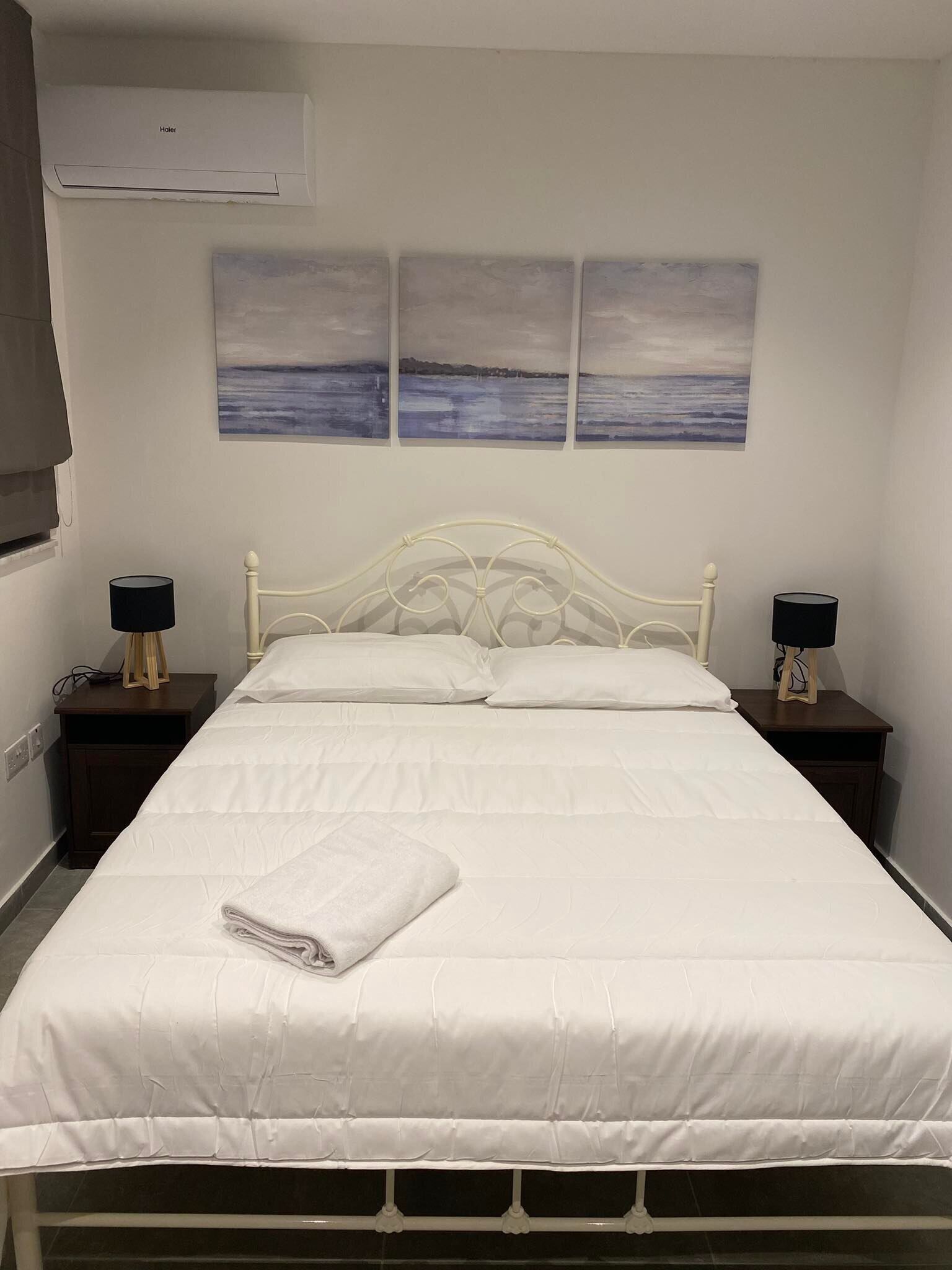 Un lit bien fait, avec du linge de lit blanc, deux tables de chevet avec des lampes et un climatiseur fixé au mur.
