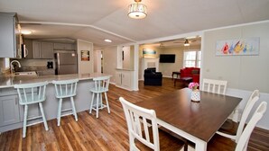 A spacious kitchen with a central island, white bar stools, a dining table with chairs, and a red sofa in the living area. - Sandy Oaks, Soundview House in Salter Path, NC! (Salter Path)