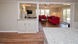 A spacious living area with a kitchen, a red sofa, and a ceiling fan. - Sandy Oaks, Soundview House in Salter Path, NC! (Salter Path)