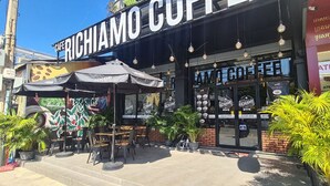 Un café con mesas al aire libre, un cartel que dice "Richiamo Coffee" y un cajero automático visible.