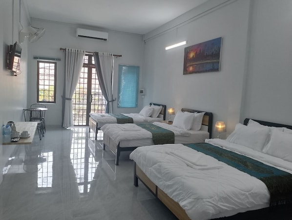 Habitación de hotel con cuatro camas, una mesa de comedor con sillas, una pequeña cocina y vistas al exterior a través de las ventanas.