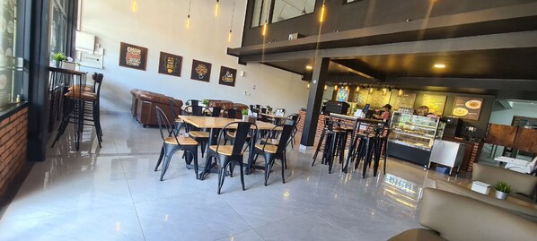 A modern cafe with multiple seating areas, including tables and chairs, and a counter with a display case.