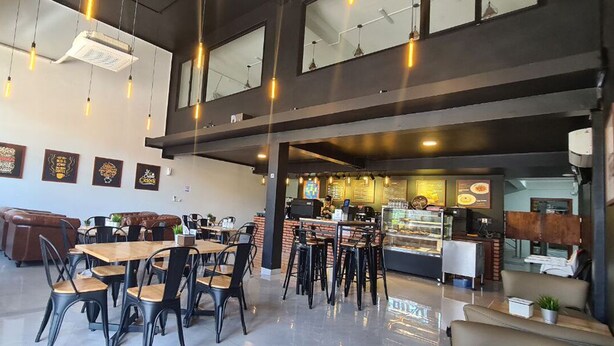 Un café moderno con varias zonas de estar, incluyendo mesas y sillas, y una barra con vitrina.