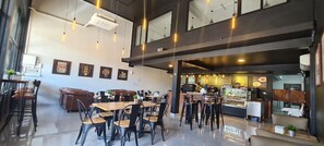 A modern cafe with multiple seating areas, including tables and chairs, and a counter with a display case.
