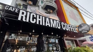 Una cafetería llamada 'RICHIMANO COFFEE' con mesas al aire libre y un balcón.
