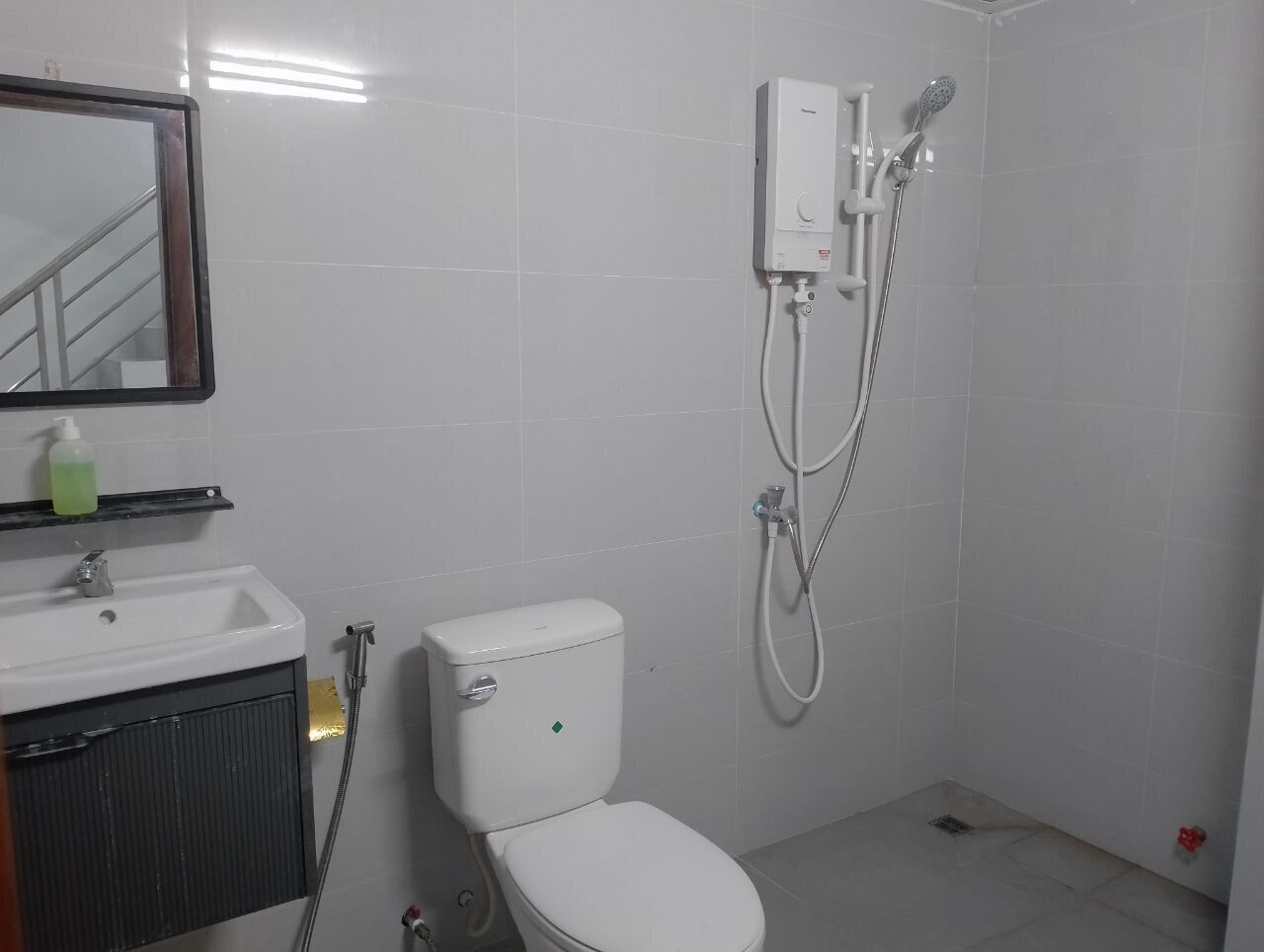 A bathroom with a toilet, sink, mirror, and a shower unit.