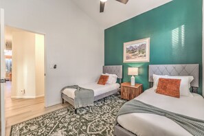 Una stanza con due letti, una parete verde decorata, un quadro con un paesaggio e un tappeto a motivi.