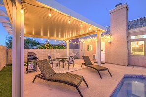 Una terrazza esterna con area salotto coperta, un barbecue e una piscina.