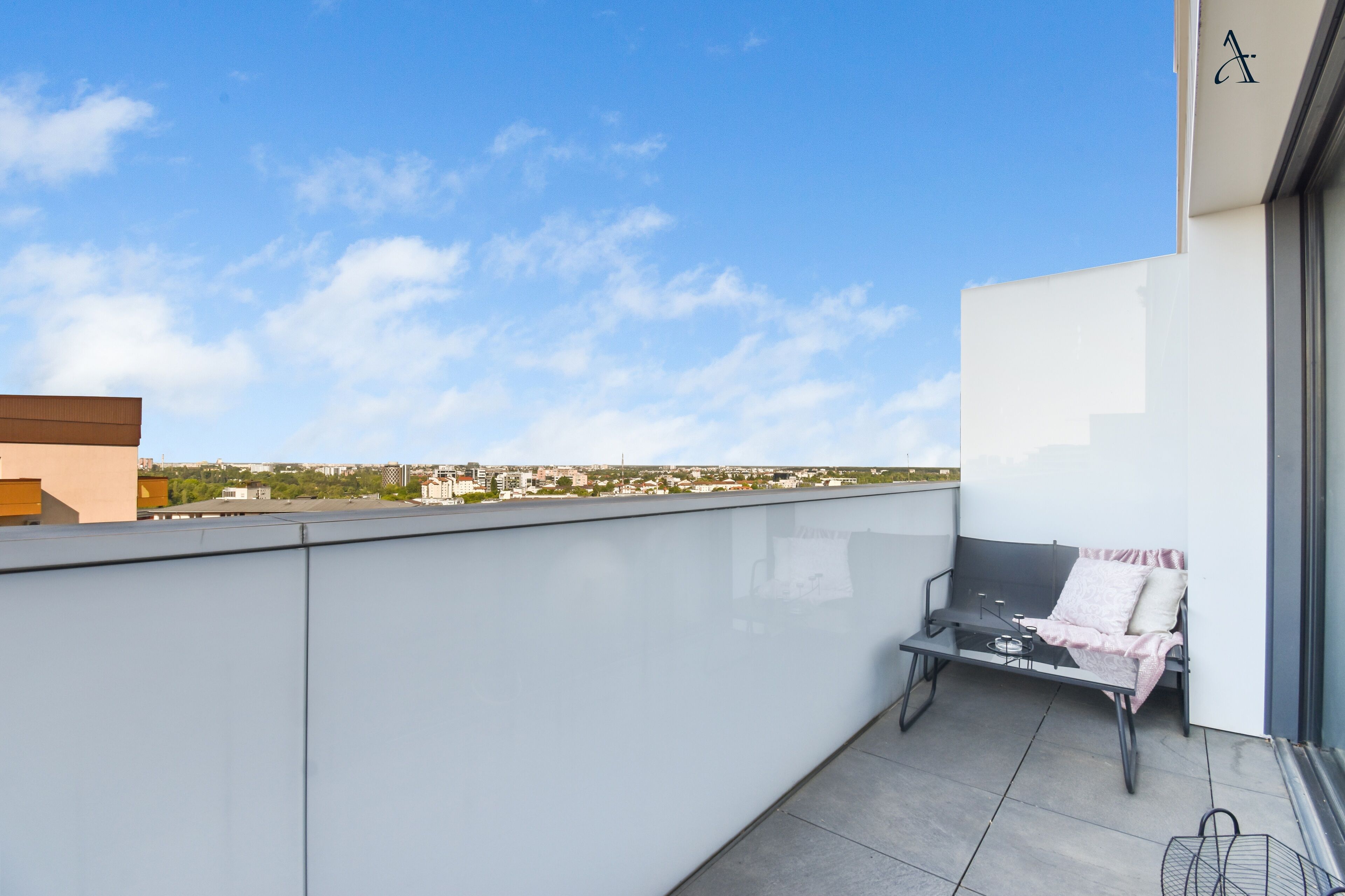 A balcony with a glass partition, a small table with a chair, and a view of the cityscape.