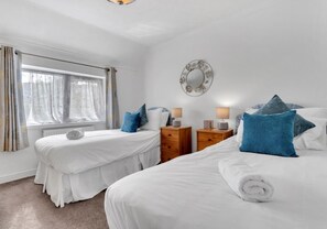 Une chambre d’hôtel avec deux lits, une fenêtre avec des rideaux, un miroir au mur et une petite table de chevet en bois avec une lampe.