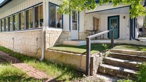 A building with stone walls, a green door, and a set of outdoor stairs leading to a covered area with a table and chairs. - Waterlily Serenity / 2 Bedroom / Creekside (Wimberley)