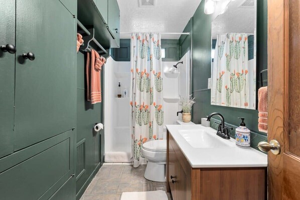 A bathroom with a white sink, green cabinets, a shower curtain with a cactus pattern, and a toilet.