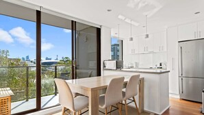 A modern kitchen with a large island, white cabinetry, and a view of the city through large windows. - Prime Location 2-Bed Apartment with Parking (Centennial Park)