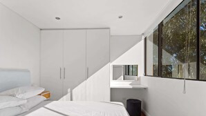 A modern bedroom with a bed, a wardrobe, a small desk, and a large window. - Prime Location 2-Bed Apartment with Parking (Centennial Park)