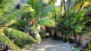 Un jardín tropical con palmeras, una estructura de techo de paja y un sendero de arena.