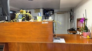 A wooden reception desk with a computer monitor, a telephone, and various items including a potted plant and a small figurine. - Budget Inn By Oyo Corpus Christi Beach (Corpus Christi)