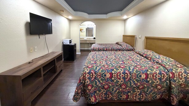 A bedroom with a bed, a TV mounted on the wall, a wooden bench, and a mirror above the sink. - Budget Inn By Oyo Corpus Christi Beach (Corpus Christi)