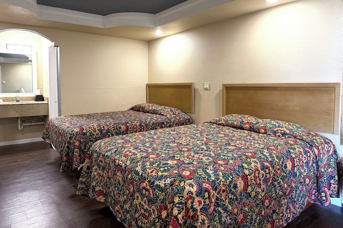 Hotellihuone, jossa on kaksi sänkyä, kylpyhuone peilillä sekä puinen pääty.