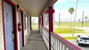 A covered corridor with red-framed doors, a fire extinguisher, and a view of a parking lot with a white SUV. - Budget Inn By Oyo Corpus Christi Beach (Corpus Christi)